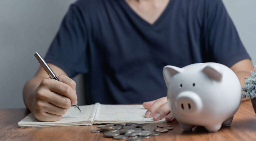 Mężczyzna piszący w zeszycie ze świnką skarbonką na pierwszym planie